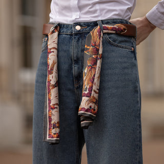 Person wearing blue jeans with a patterned pheasant scarf and leather belt, and white shirt, blurred background