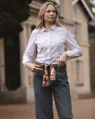 Woman wearing a white shirt and dark jeans with a leather scarf belt, standing outdoors.